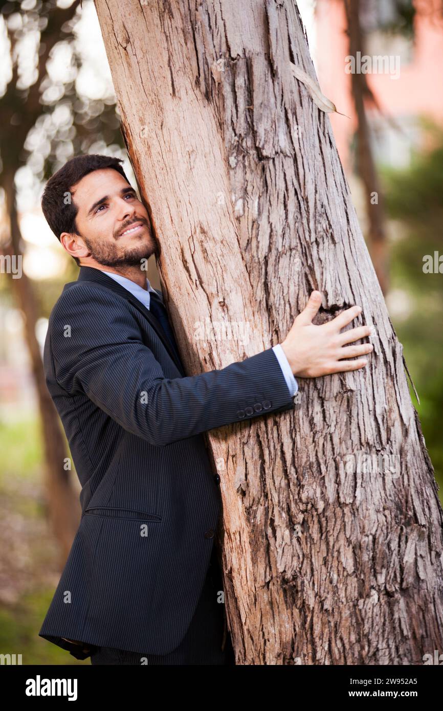 Uomo d'affari abbracci un tronco di albero Foto Stock