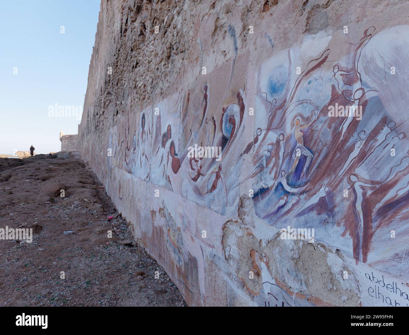 Bellissime opere d'arte sulle mura cittadine della Medina mentre qualcuno cammina lungo la spiaggia rocciosa di Essaouira, in Marocco. 23 dicembre 2023 Foto Stock