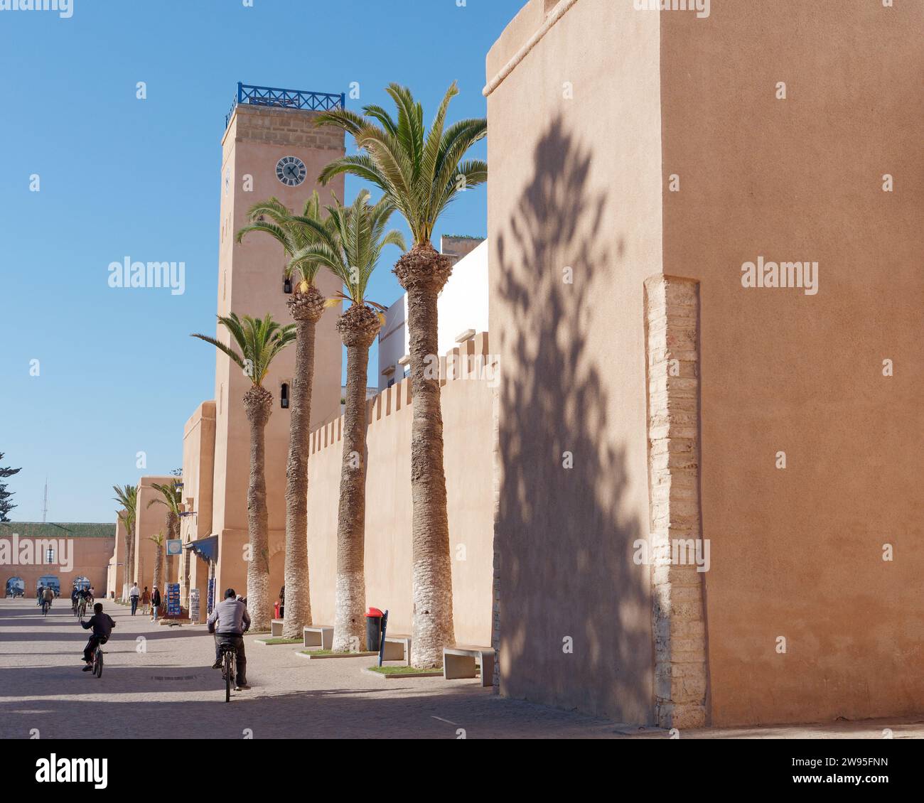 Strada principale nella medina di Essaouira con torre dell'orologio, palme e ciclisti, Marocco. 23 dicembre 2023 Foto Stock