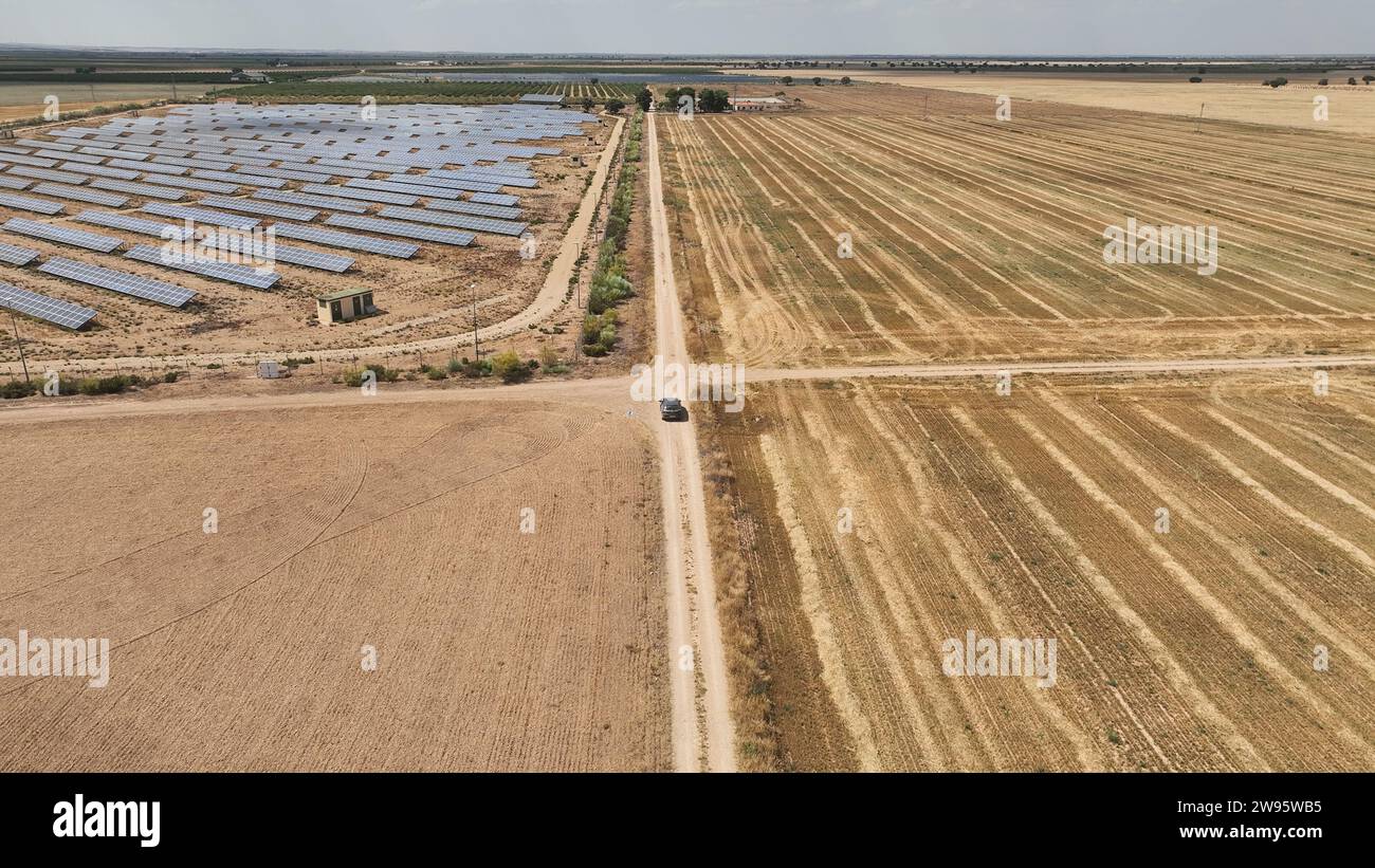 Vista aerea di un'auto che viaggia su strade sterrate tra grandi distese di campi coltivati e impianti fotovoltaici. Attraversamento di strade sterrate Foto Stock