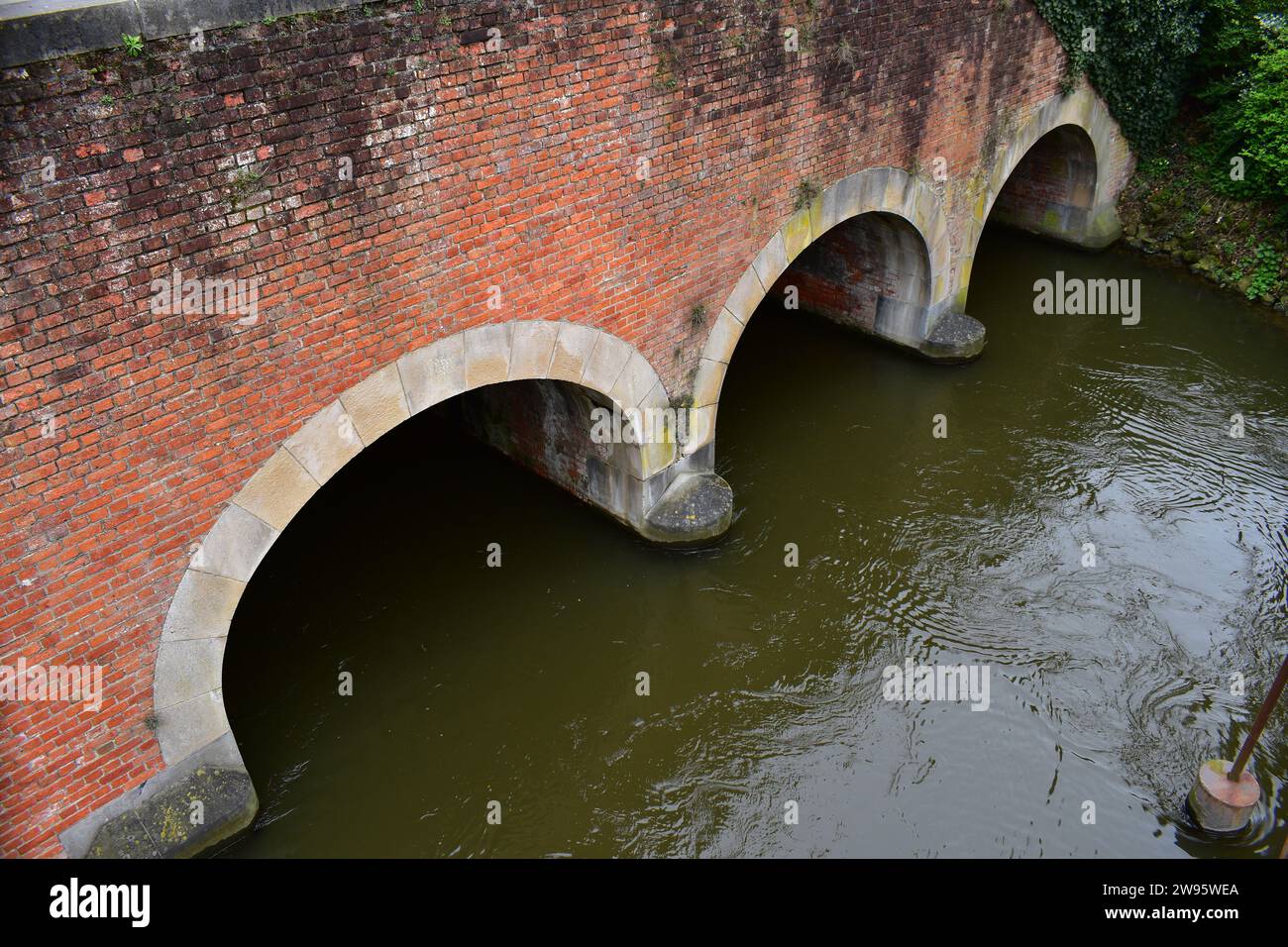 L'acqua scorre sotto il ponte in mattoni dello Smedenpoort, una delle porte medievali della città che circondano il centro di Bruges Foto Stock