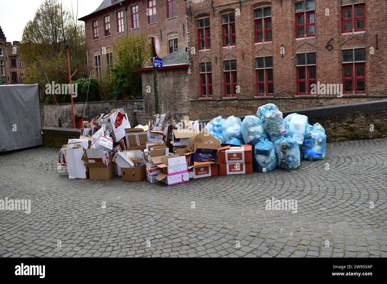 Una grande pila di scatole di cartone e sacchetti di plastica blu contenenti lattine e rifiuti di plastica in attesa della raccolta dei rifiuti nel centro della città di Bruges Foto Stock