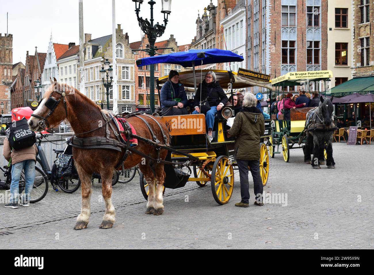 I turisti fanno un tour "il carrozza a cavallo di Bruges" in una carrozza di legno trainata da un cavallo sulla Grand Place nel centro medievale della città di Bruges Foto Stock