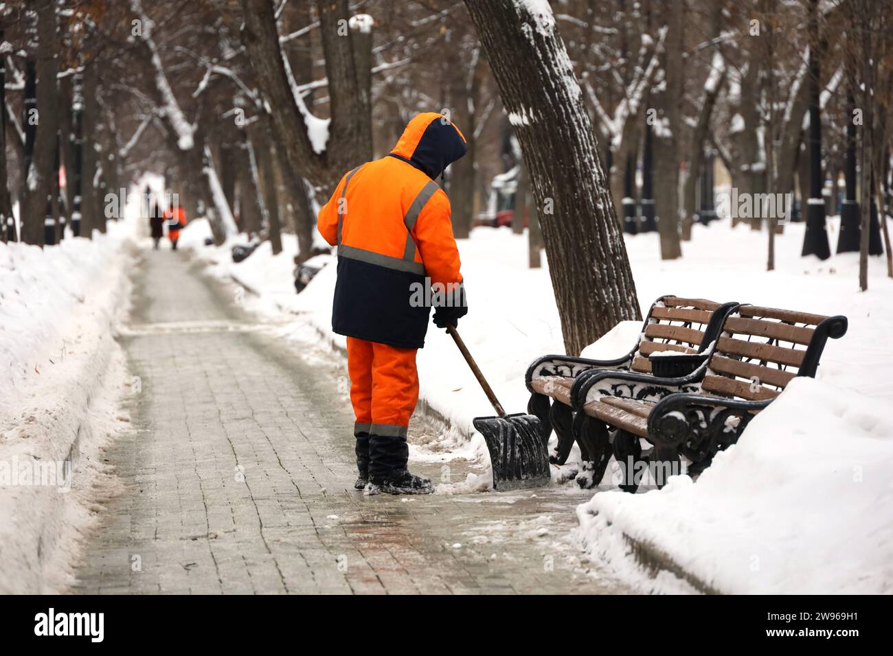 Operaio dei servizi comunali in uniforme con una pala libera la neve su un marciapiede. Uomo durante la rimozione della neve nelle città invernali, pulizia delle strade Foto Stock