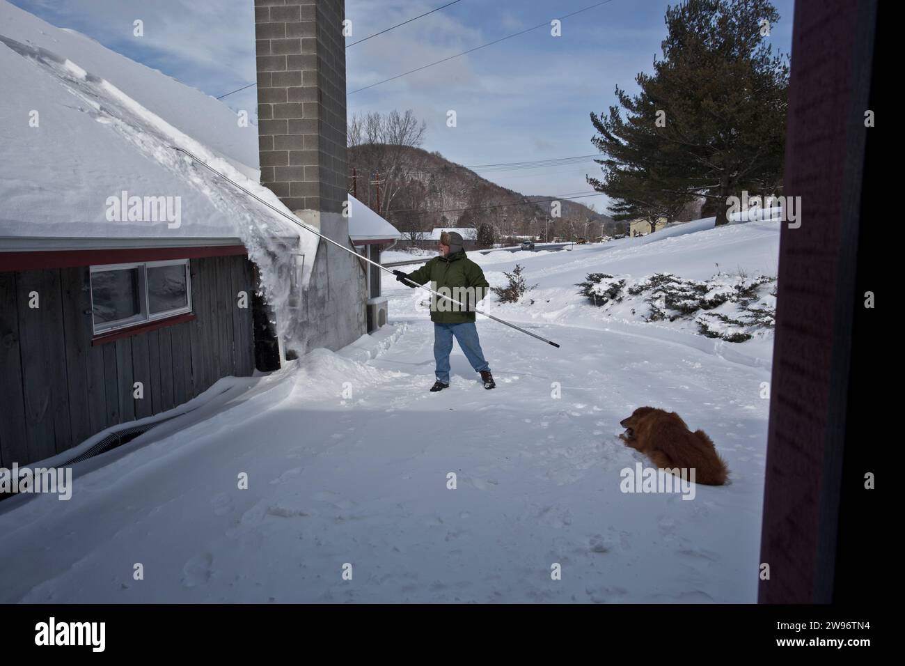 Un uomo rastrella una pesante nevicata dal tetto della sua casa nel Vermont meridionale Foto Stock