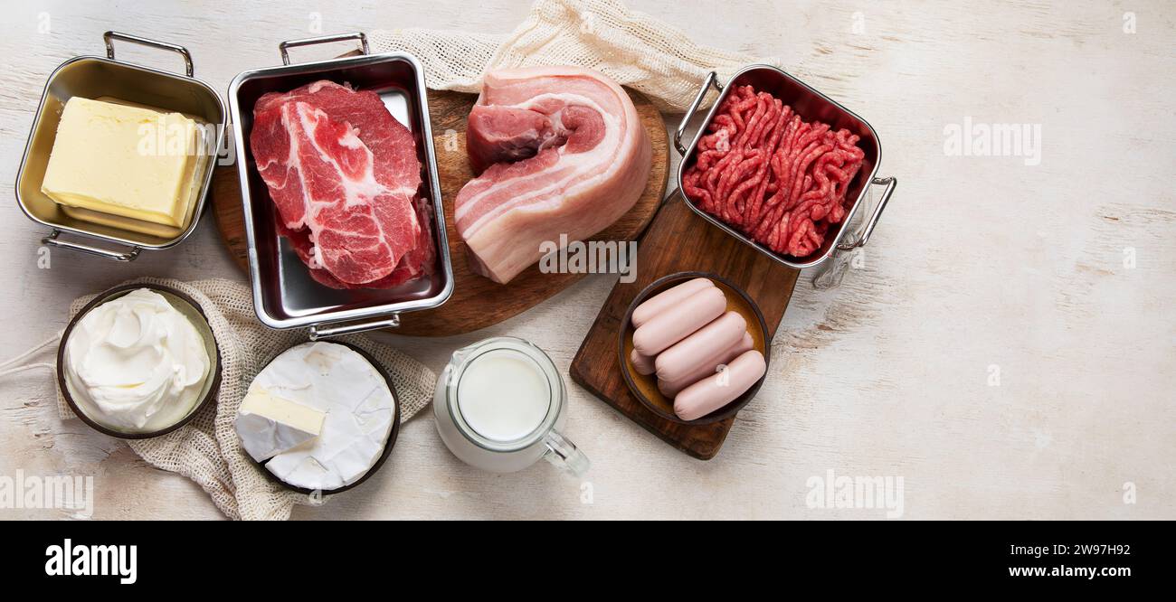 Grassi saturi sui tavoli. Carne cruda, salsicce, formaggio, burro. Cattivo concetto di cibo. Vista dall'alto, banner, spazio di copia. Foto Stock