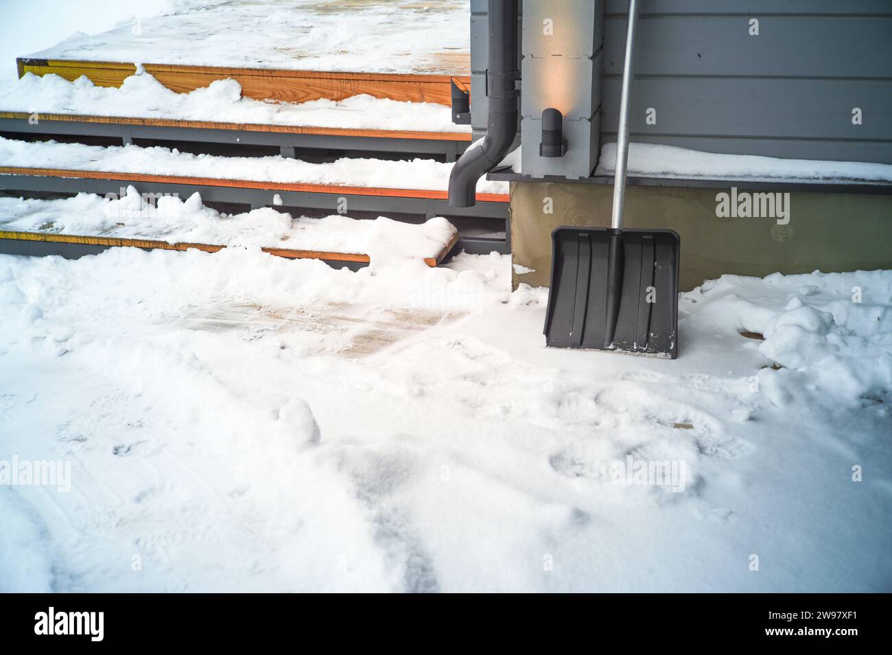 una pala appoggiata contro il muro di una casa moderna, scena invernale Foto Stock