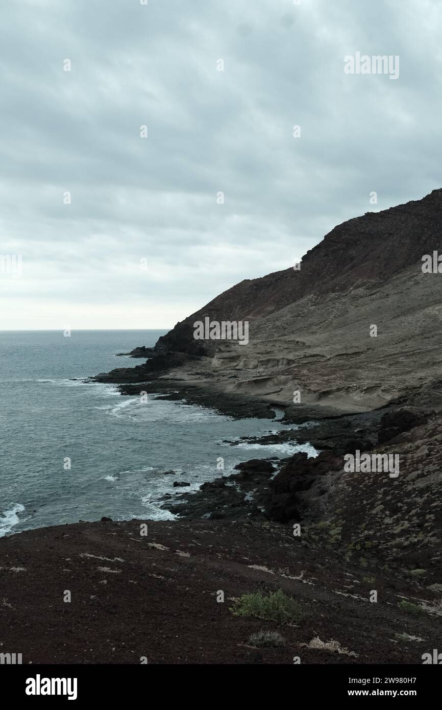 Un tranquillo paesaggio marino caratterizzato da una spiaggia con formazioni rocciose e lussureggiante erba verde, che si estende dal bordo dell'oceano alla spiaggia sabbiosa Foto Stock