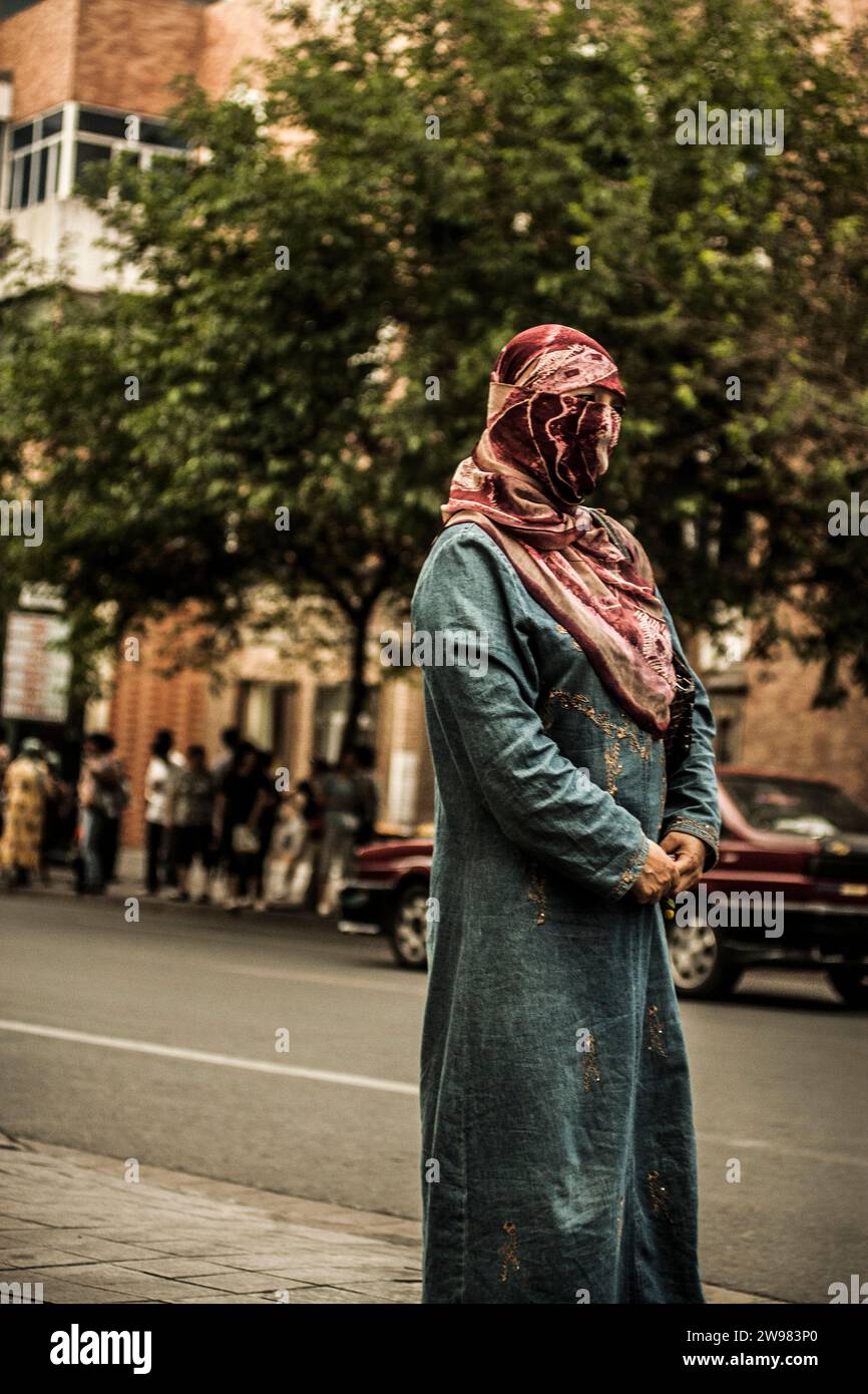 Donna musulmana uigura in piedi su un marciapiede. Foto Stock
