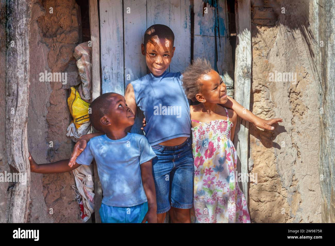 ritratto di un gruppo di bambini africani nel villaggio, in piedi di fronte alla porta della capanna in un insediamento informale Foto Stock