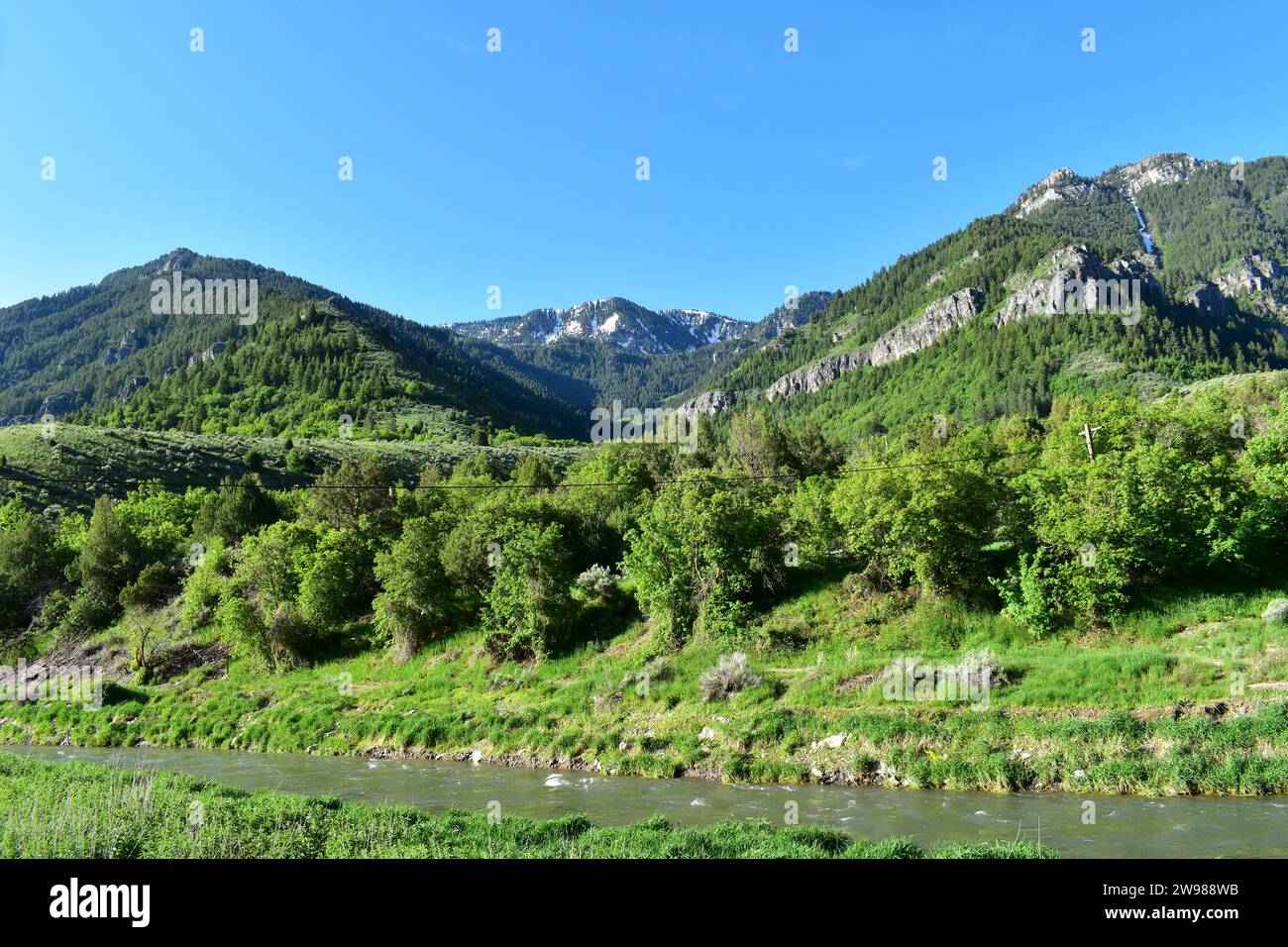 Vista panoramica della natura di un flusso d'acqua che scorre attraverso la campagna con le maestose vette delle Montagne Rocciose sullo sfondo nello Utah Foto Stock