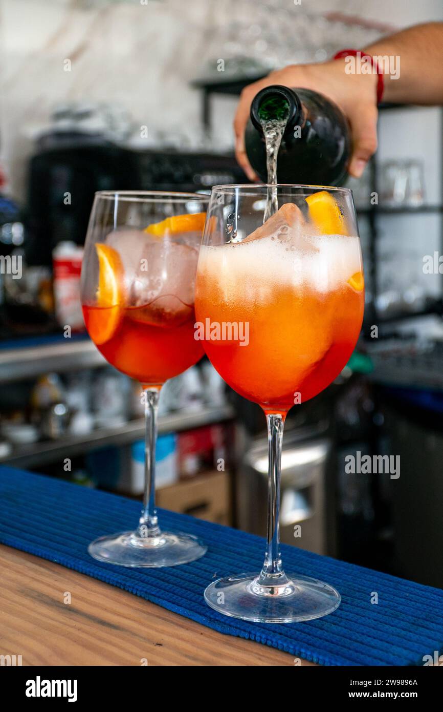 Un barista che aggiunge prosecco a un paio di cocktail italiani Aperol spritz Foto Stock