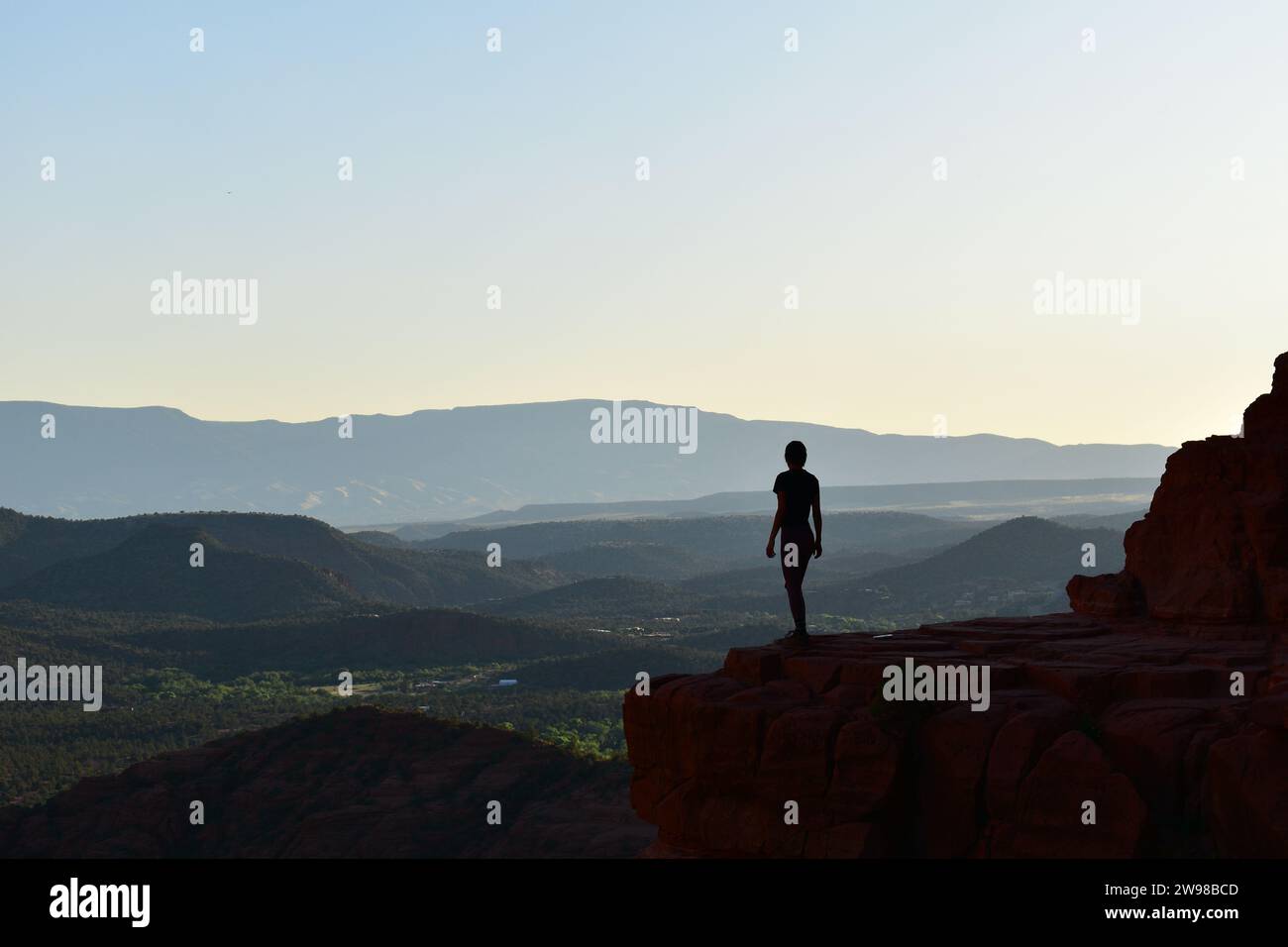 Silhouette di una persona in piedi su una sporgenza di pietra che si affaccia sul paesaggio desertico dell'Arizona dalla Cathedral Rock di Sedona, Arizona Foto Stock