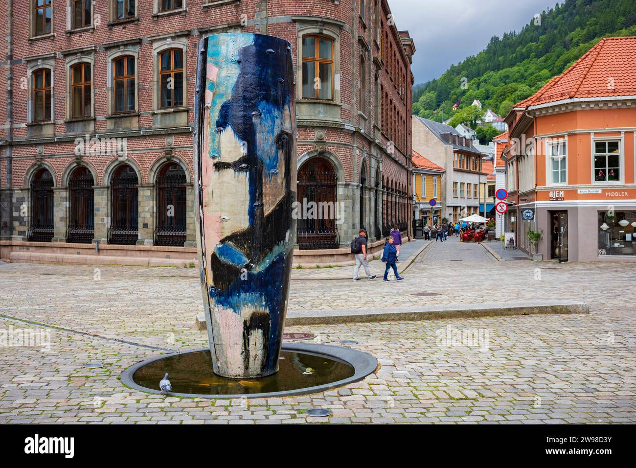 Bergen, Norvegia, 22 giugno 2023: Un gruppo di persone cammina su una strada acciottolata vuota nel centro della città di Bergen dopo un temporale. Un vesse in ceramica Foto Stock