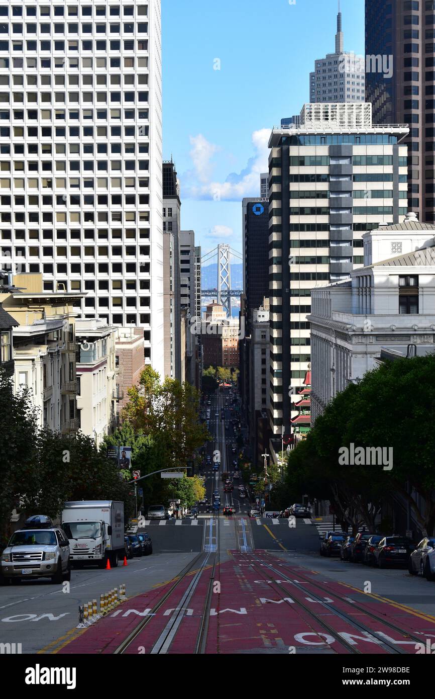 Una vista della ripida discesa di California Street con il Bay Bridge sullo sfondo nel centro di San Francisco Foto Stock