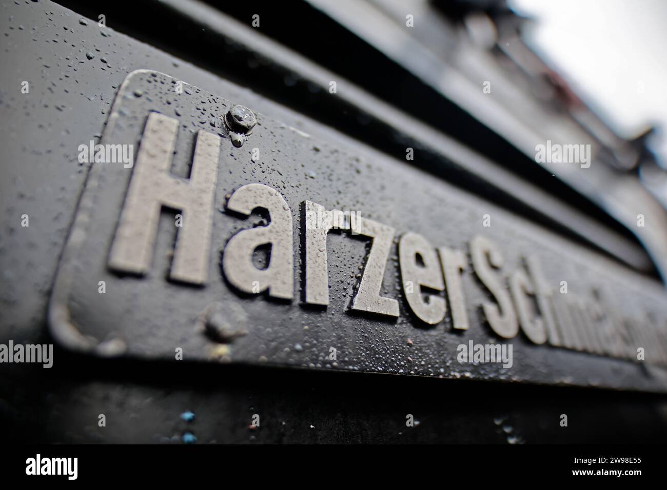 Schierke, Germania. 25 dicembre 2023. Gocce di pioggia si aggrappano a un cartello della locomotiva Harzer Schmalspurbahnen GmbH presso la stazione di Schierke. Il tempo piovoso sta anche influenzando il turismo nelle montagne Harz. A causa del tempo instabile con pioggia e tempeste, l'HSB ha anche sospeso i servizi ferroviari per il Brocken il giorno di Natale. I passeggeri possono viaggiare sulla linea ferroviaria fino a Schierke. Crediti: Matthias Bein/dpa/Alamy Live News Foto Stock