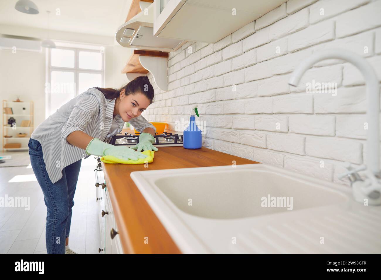 Donna impegnata nella pulizia e spolveratura di mobili da cucina a casa Foto Stock