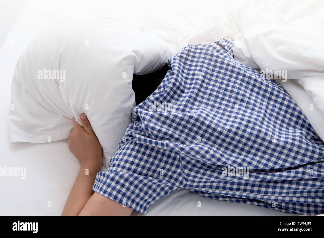 Donna esausta che copre la testa con un cuscino a causa dell'insonnia e di rumori fastidiosi Foto Stock