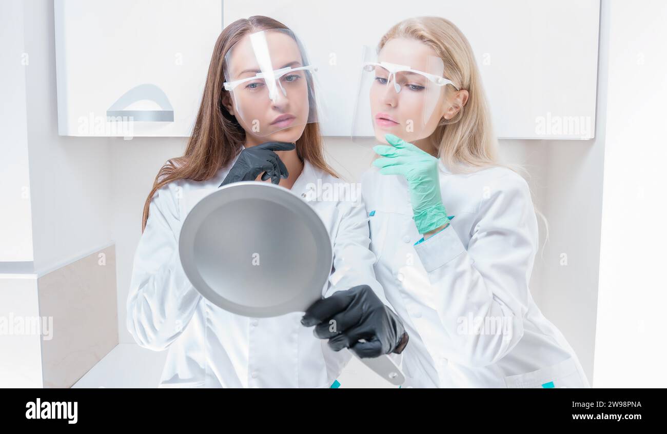 Due estetiste posano in un salone medico con uno specchio in mano. Concetto di ringiovanimento. Supporti misti Foto Stock
