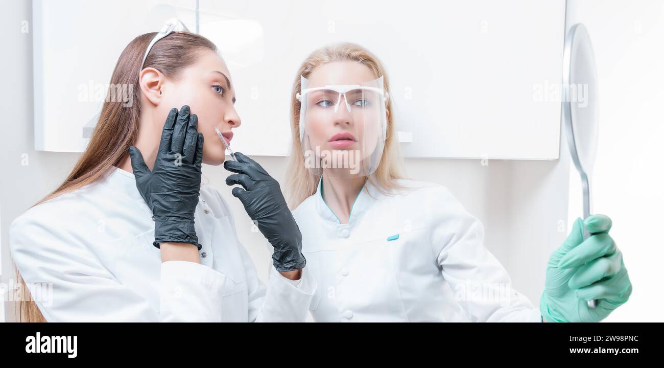 Due estetiste posano in un salone medico con uno specchio in mano. Concetto di ringiovanimento. Supporti misti Foto Stock