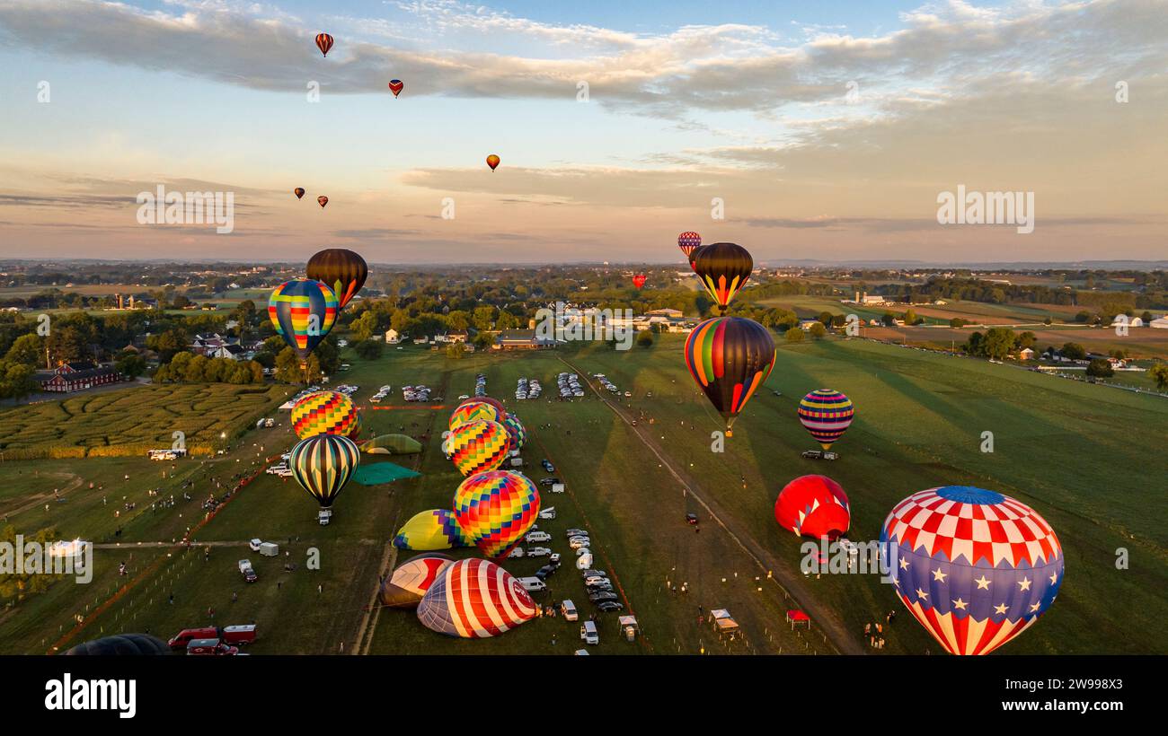 Vista aerea delle mongolfiere in un meraviglioso cielo al tramonto, che galleggia su un lussureggiante campo verde di erba e campi di mais durante un festival Foto Stock