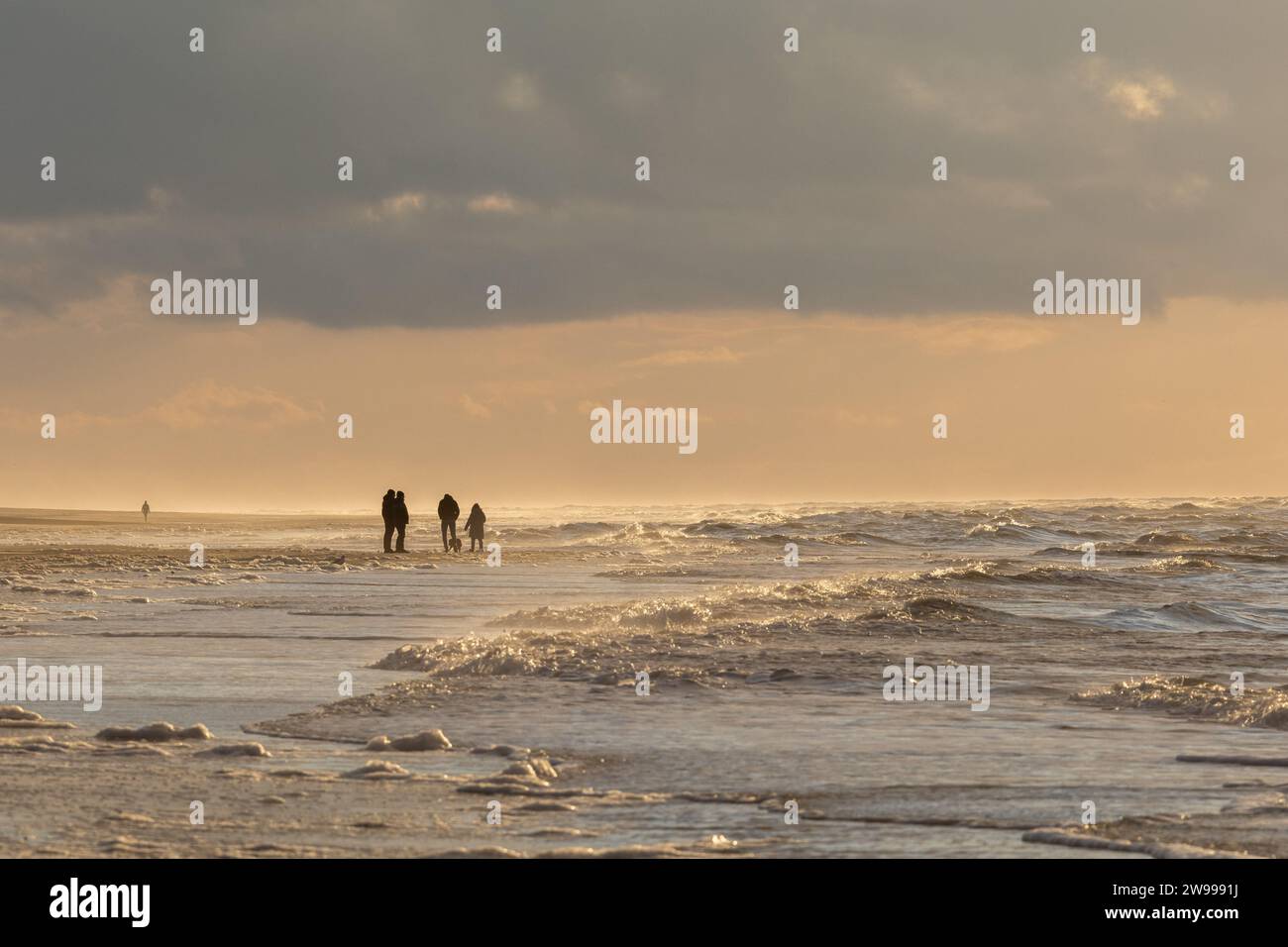 Un gruppo di persone che si divertono a fare una passeggiata serale lungo la spiaggia, illuminata da un bellissimo tramonto Foto Stock