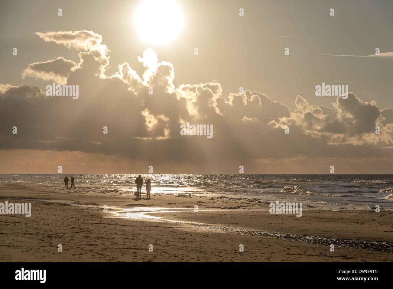 Un gruppo di persone che si divertono a fare una passeggiata serale lungo la spiaggia, illuminata da un bellissimo tramonto Foto Stock