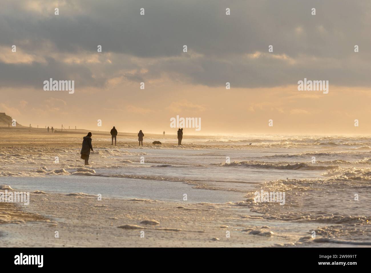 Un gruppo di persone che si divertono a fare una passeggiata serale lungo la spiaggia, illuminata da un bellissimo tramonto Foto Stock