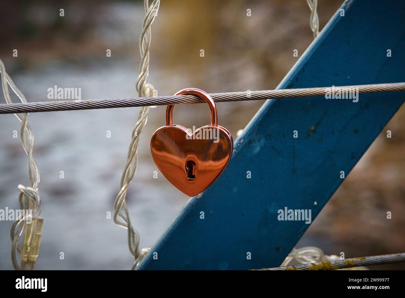Un lucchetto a forma di cuore attaccato a una recinzione vicino a un corpo d'acqua. Foto Stock