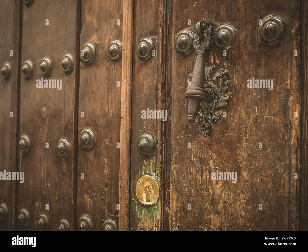 Una vecchia porta di legno usurata con rivetti in metallo e battito nero a Siviglia, Andalusia, Spagna Foto Stock