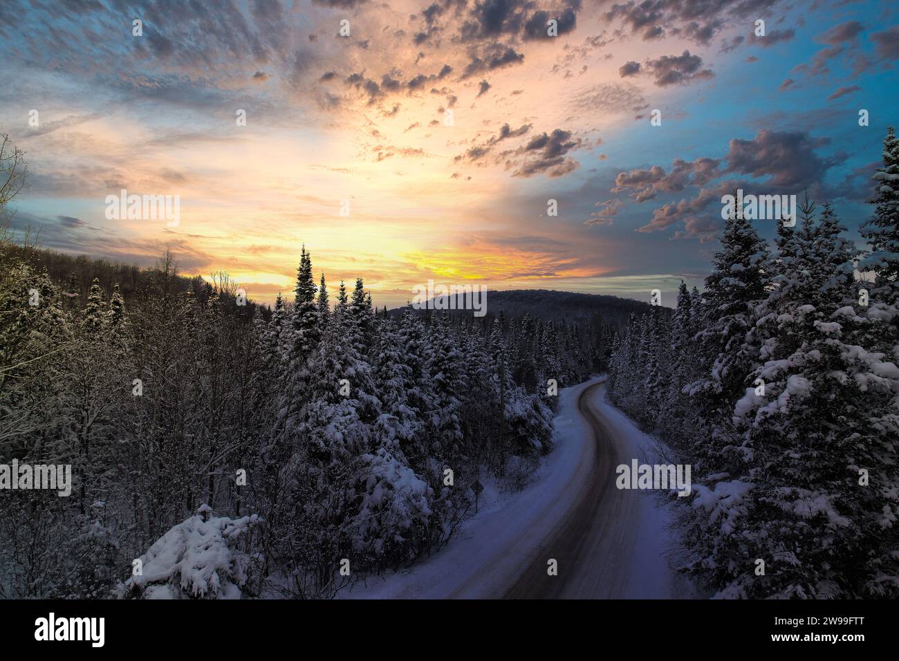 Un paesaggio invernale panoramico caratterizzato da una strada innevata che attraversa la foresta. Laurentides, Quebec Foto Stock