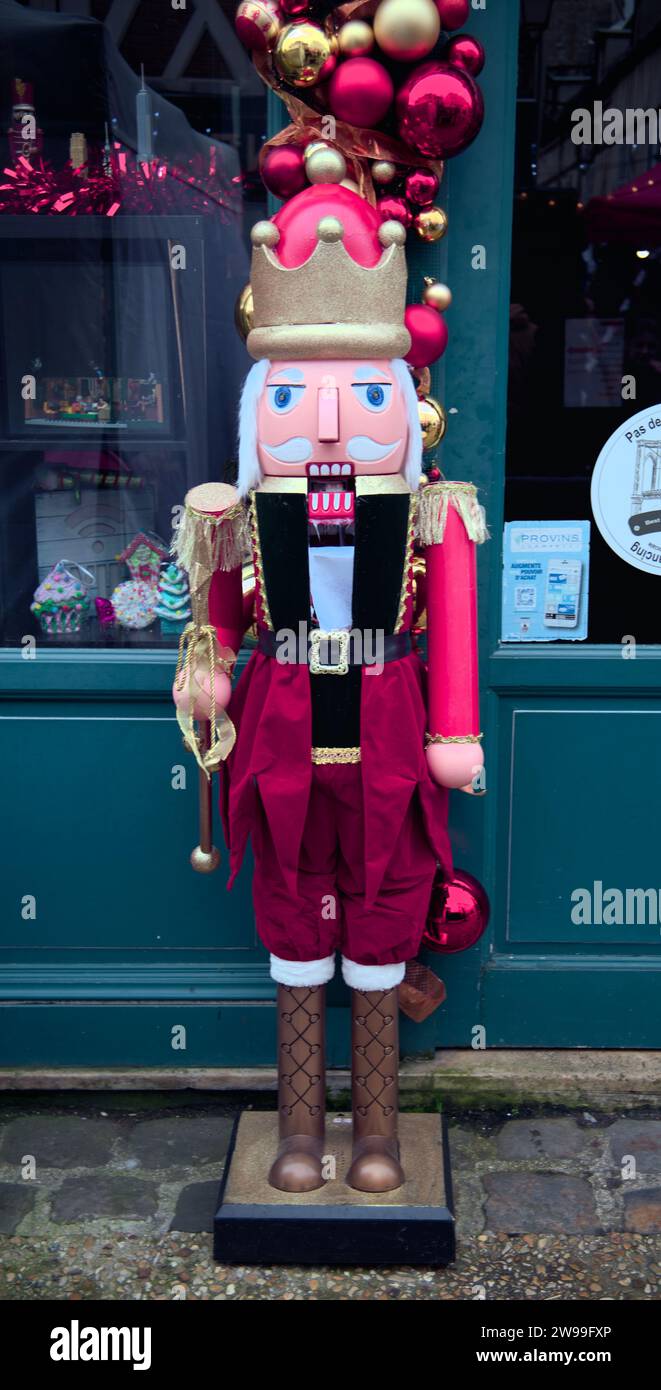 Una statuetta dello schiaccianoci rosso e bianco che indossa un abito tradizionale, decorata con ornamenti festivi, in piedi su una superficie di colore chiaro Foto Stock