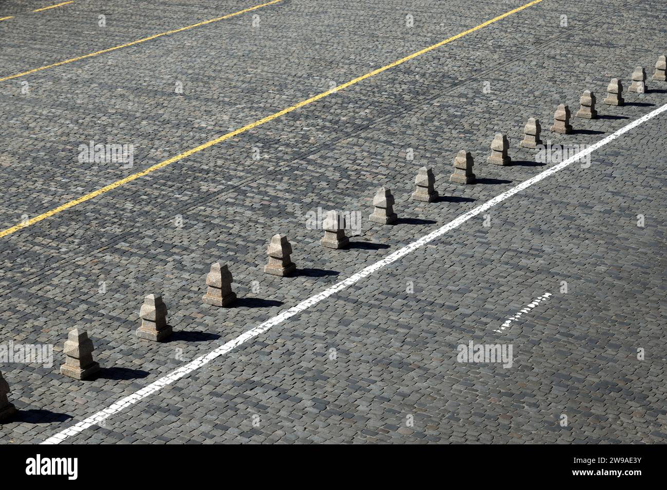 Barriera dalle piramidi di granito dopo una lunga linea bianca sulla vista laterale della pavimentazione stradale in pietra Foto Stock
