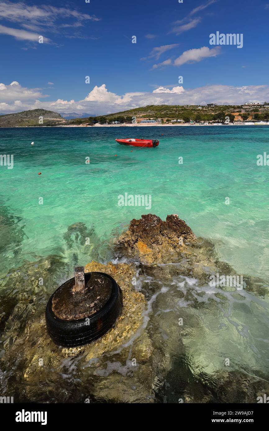 176 ormeggio fatto di una vecchia gomma alla spiaggia di Rilinda, barca fuoribordo rossa sullo sfondo, villaggio di Ksamil. Sarande-Albania. Foto Stock