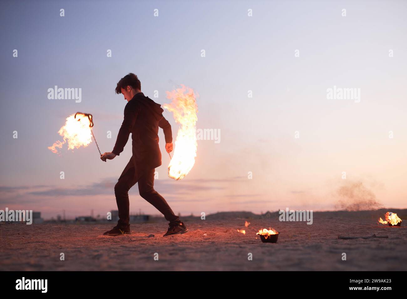 Vista laterale completa dello spettacolo di fuoco maschile che danzano con le fiamme nella natura durante il tramonto, spazio copia Foto Stock