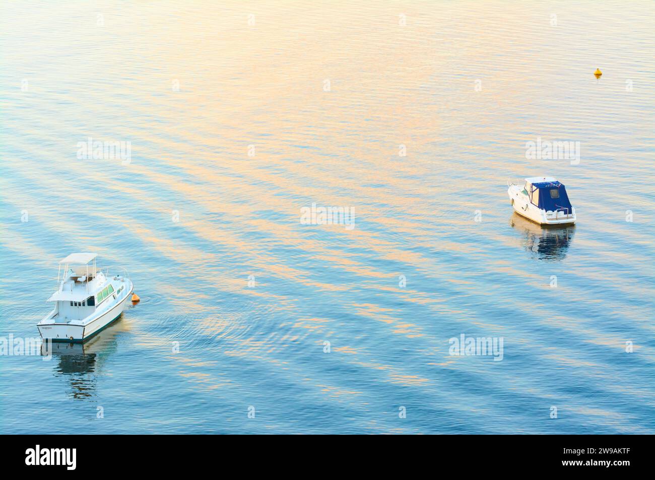 Due barche a Mosman Bay sul fiume Swan al tramonto con ondulazioni che riflettono i colori blu e peachy del tramonto, Perth, Australia Occidentale. Foto Stock
