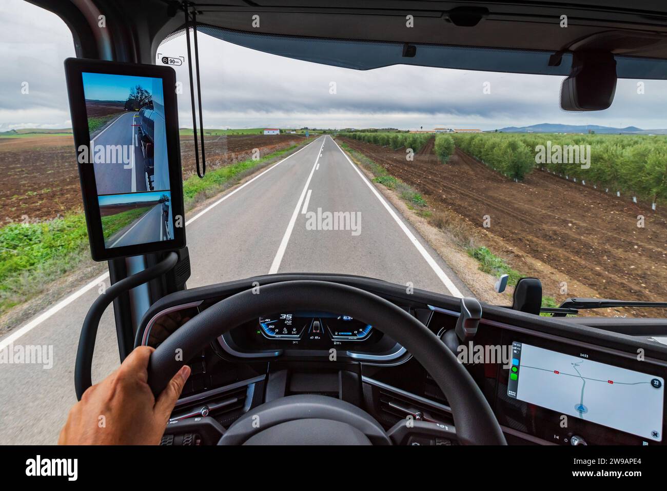 Visualizzare dalla posizione del conducente di un autocarro una strada nel mezzo dei campi coltivati e il conducente guidato dal GPS sullo schermo del cruscotto. Foto Stock