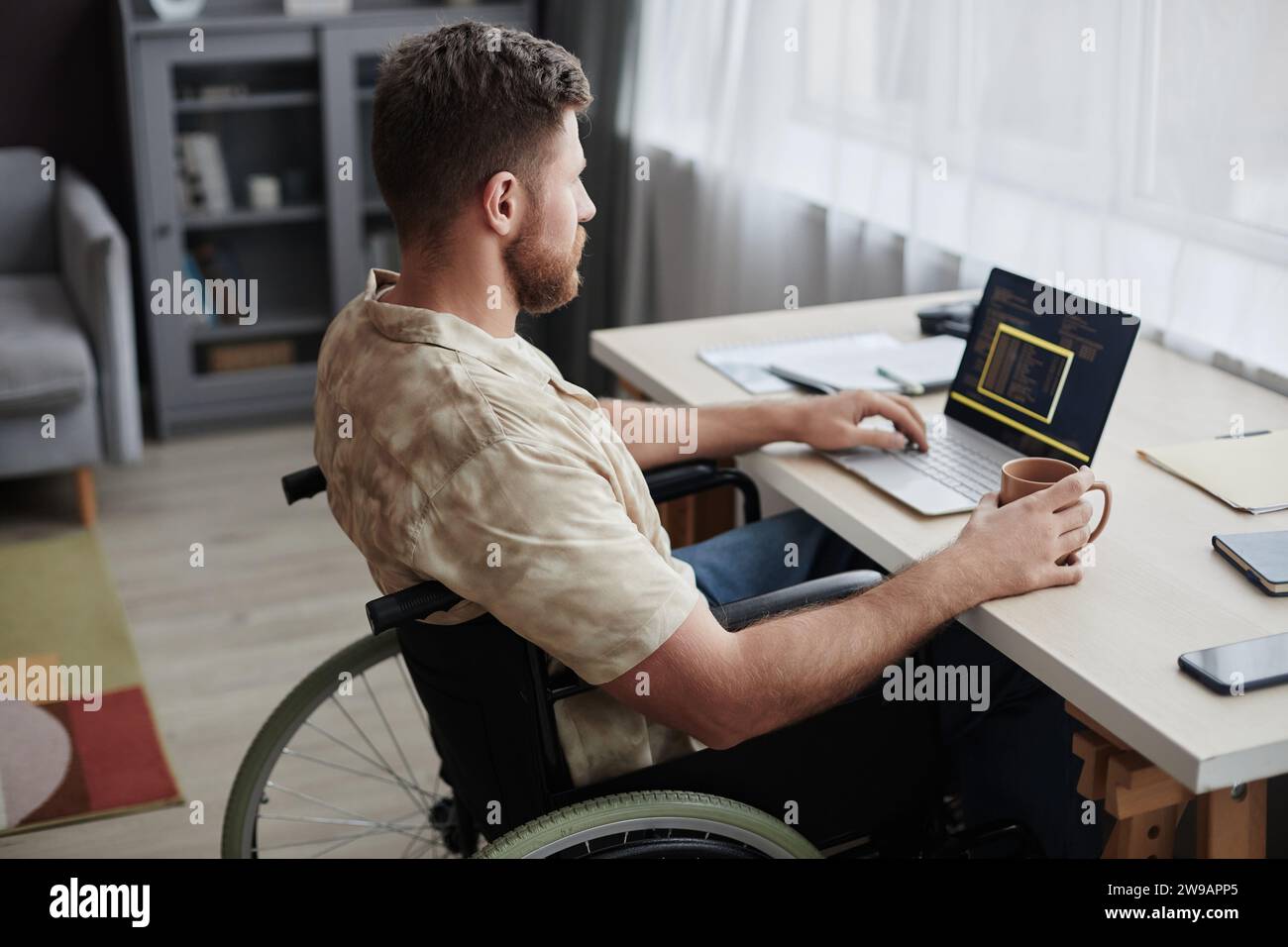 Ritratto laterale di un uomo barbuto con disabilità che usa il computer mentre lavora da casa in carriera IT Foto Stock