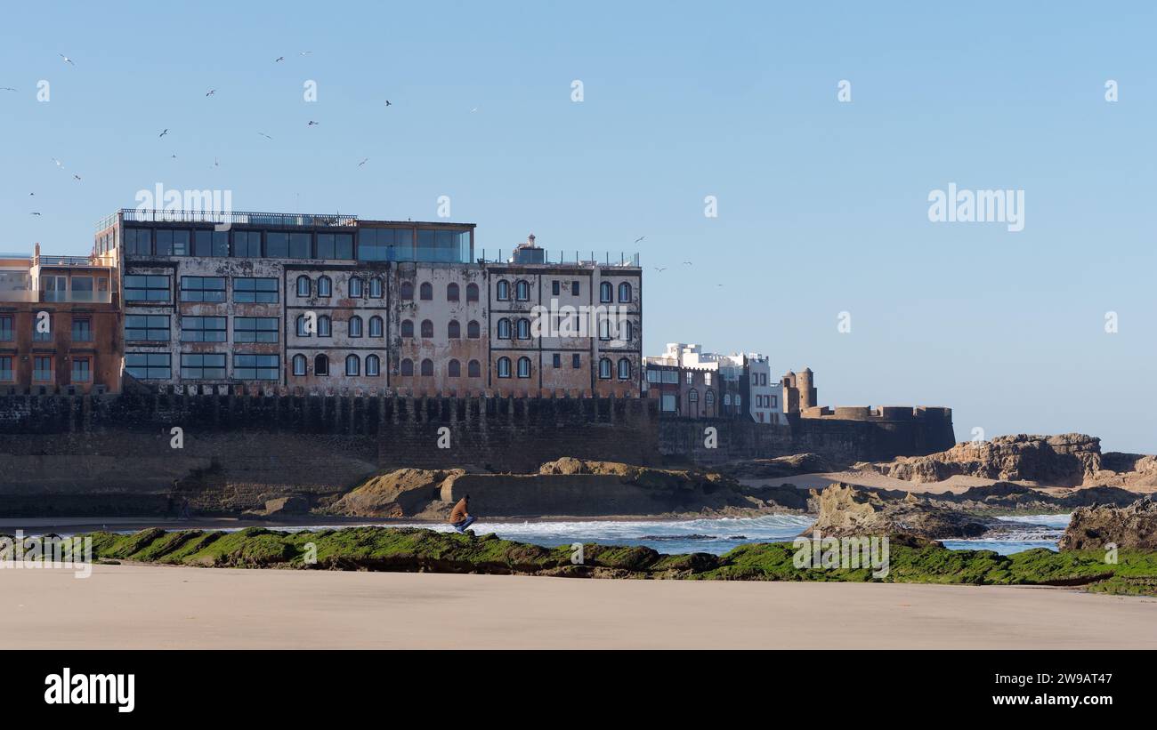 Man siede sulla costa rocciosa ricoperta di muschio accanto alla storica Medina e alla fortezza di Essaouira, in Marocco. 26 dicembre 2023 Foto Stock