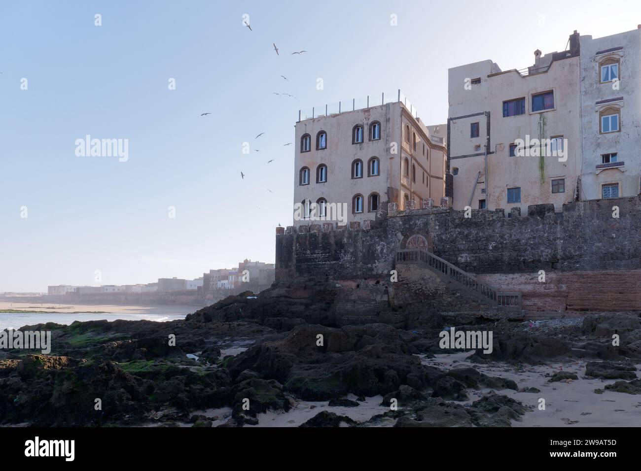 Parte delle mura della città e della storica Medina con costa rocciosa e spiaggia alle spalle a Essaouira, Marocco. 26 dicembre 2023 Foto Stock
