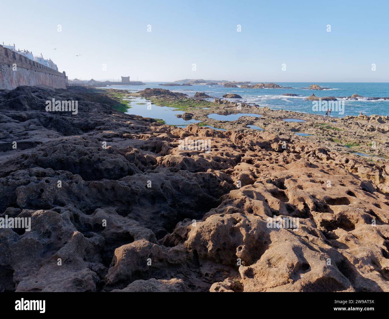 Costa rocciosa frastagliata con piscine di marea a Essaouira con parte della medina rimasta, Marocco. 26 dicembre 2023 Foto Stock