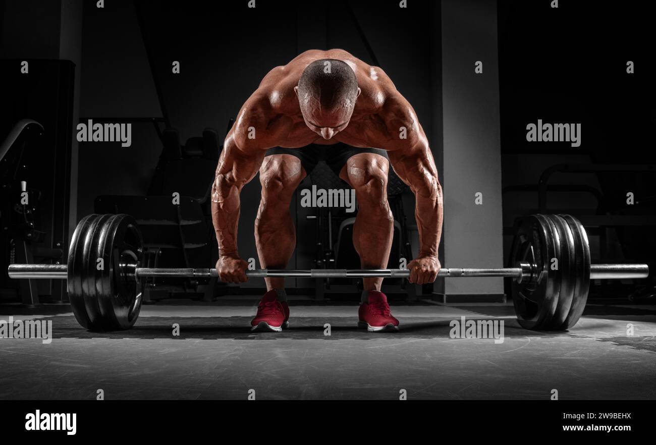 L'uomo muscoloso è incerto con un campanello tra le mani. Deadlift. Concetto di allestimento e sollevamento potenziato. Supporti misti Foto Stock