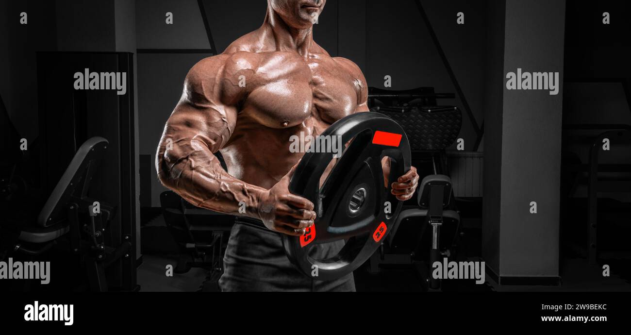 Uomo muscoloso che posa in palestra con un disco a campana. Concetto di allestimento e sollevamento potenziato. Supporti misti Foto Stock
