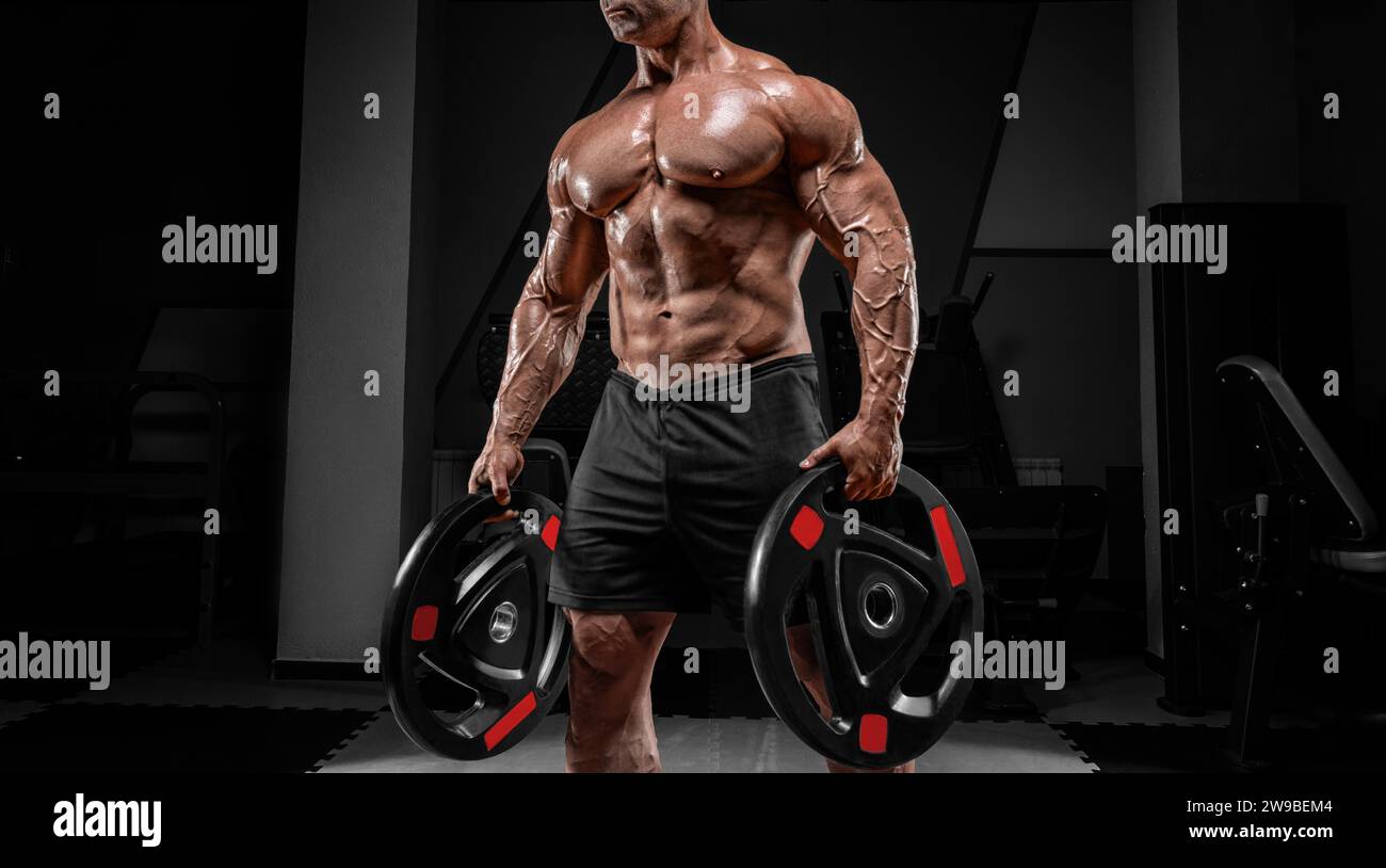 L'uomo muscoloso si trova in una palestra con dischi a campana. Concetto di allestimento e sollevamento potenziato. Supporti misti Foto Stock