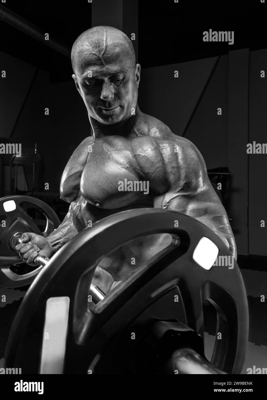 Sollevatore professionista che posa in palestra con un campanello tra le mani. Bodybuilding classico. Supporti misti Foto Stock