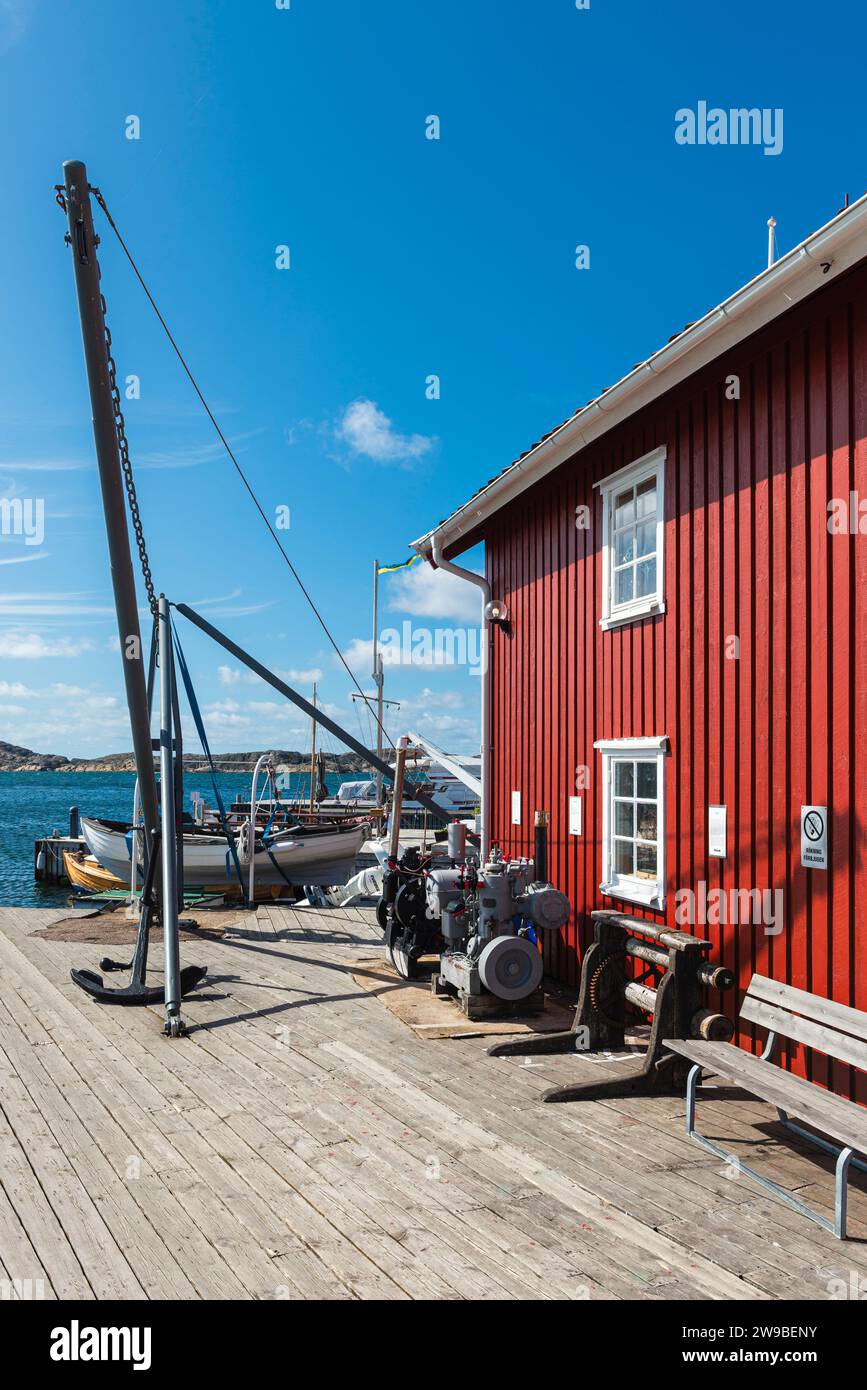 Magazzini con tipiche facciate in legno rosso e barche da pesca nel porto di Skärhamn nell'arcipelago dell'isola di Tjörn in estate, Svezia Foto Stock