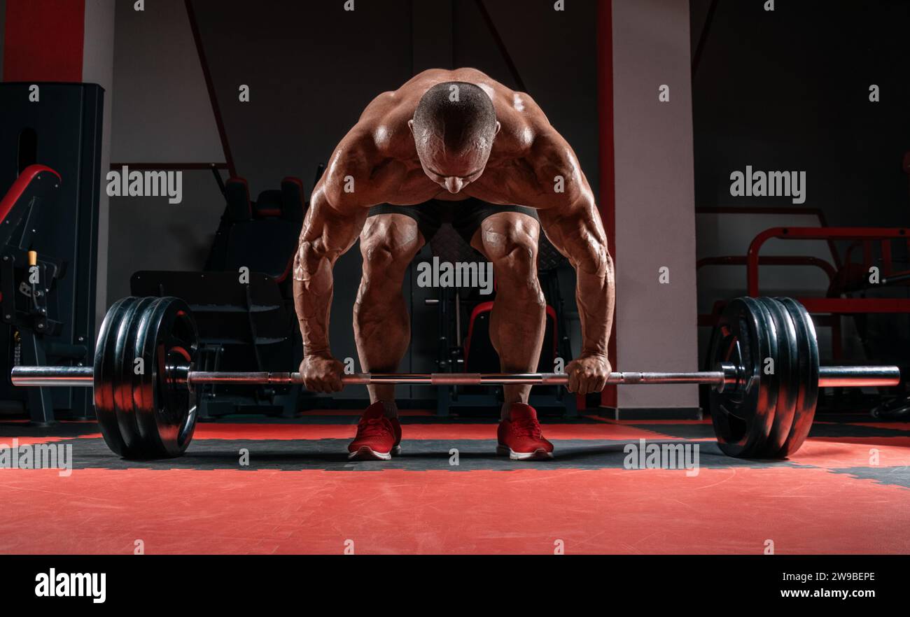 L'uomo muscoloso è incerto con un campanello tra le mani. Deadlift. Concetto di allestimento e sollevamento potenziato. Supporti misti Foto Stock