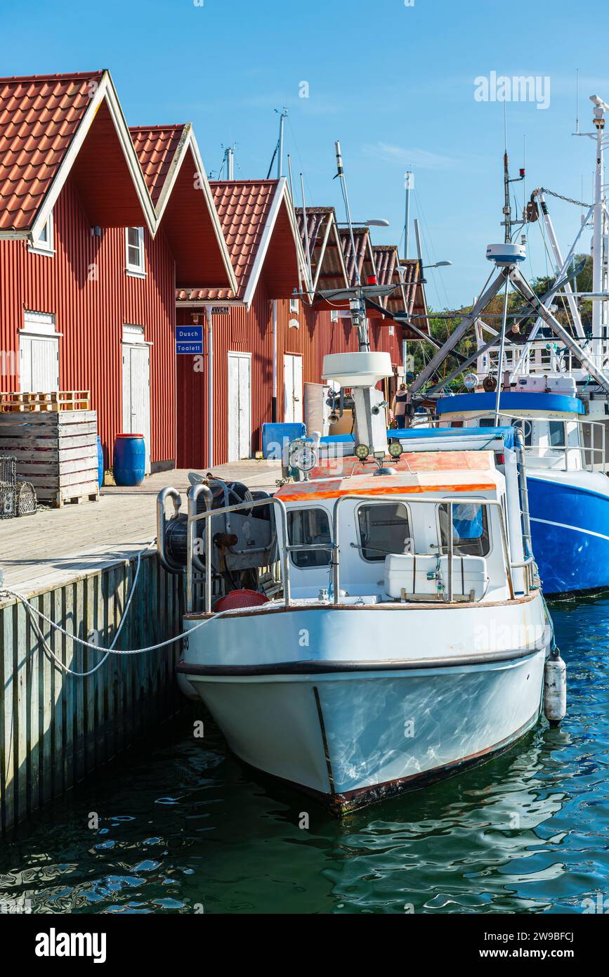 Magazzini con tipiche facciate in legno rosso e barche da pesca nel porto di Skärhamn nell'arcipelago dell'isola di Tjörn in estate, Svezia Foto Stock