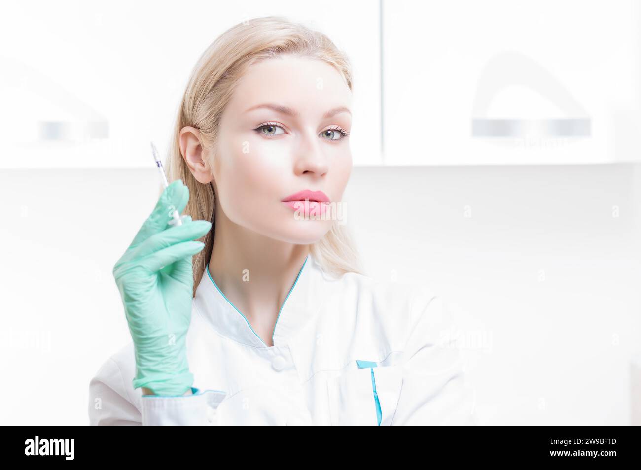 Ritratto di una ragazza bionda in abito medico con una siringa in mano. Pubblicità del centro medico. Supporti misti Foto Stock