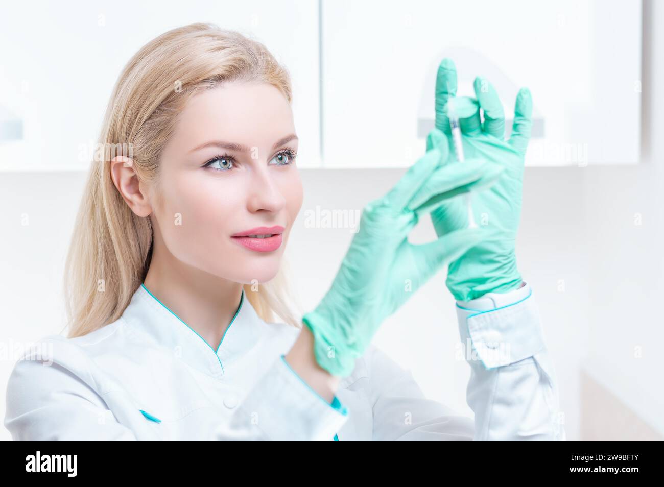 Ritratto di una ragazza bionda in abito medico con una siringa in mano. Pubblicità del centro medico. Supporti misti Foto Stock